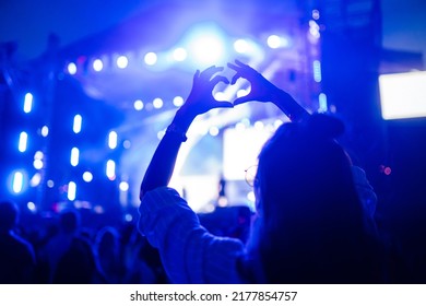 Heart shaped hands at concert, loving the artist and the festival. Music concert with lights and silhouette of people enjoying the concert.
