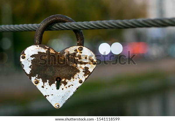 Heart shaped heavy rusty antique lock on urban\
street background. Vintage padlock on rope. Romantic love concept,\
fading away feelings of\
love.