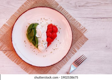 Heart shaped Italian Caprese Salad arranged by Italian basil,buffalo mozzarella and tomatoes look like Italian Flag on plate with white wood table background.Love Italian food concept for Valentine 