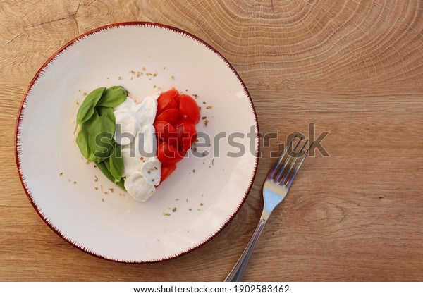 Heart shaped Italian Caprese Salad arranged by Italian\
basil,buffalo mozzarella and tomatoes look like Italian Flag on\
plate with wooden table background.Love Italian food concept for\
Valentine day 