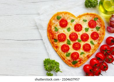 Heart shaped Italian margherita pizza with tomatoes,mozzarella cheeses and parsley on parchment paper with wooden background.Love vegetarian food concept for Valentine's day.Top view.copy space

