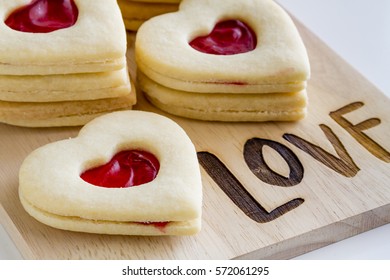 Heart shaped linzer cookies filled with strawberry jam sitting on wooden cutting board with word love etched in wood