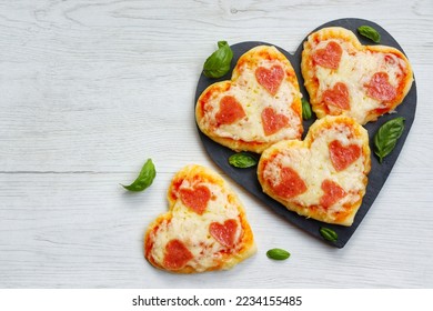 Heart shaped mini pizzas with heart shaped pepperoni on heart shaped slate plate with white wood background.Creative art food idea for celebrate Valentine or Mother day.Top view.Copy space - Powered by Shutterstock