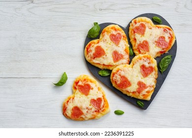 Heart shaped mini pizzas with heart shaped pepperoni on heart shaped slate plate with white wood background.Creative art food idea for celebrate Valentine or Mother day.Top view.Copy space - Powered by Shutterstock