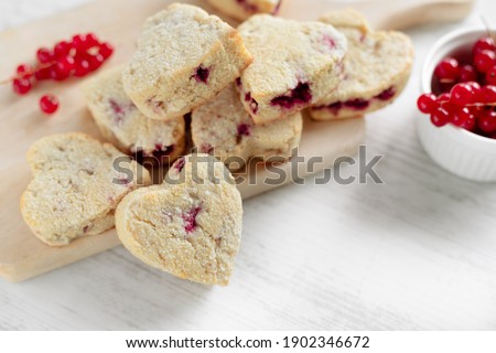 Heart shaped red currant scones, healthy sweet coconut flour cookies on wooden cutting board and white table surface, Valentine's Day sweet treats front close up