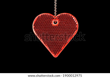 Heart shaped reflector on chain isolated on black background. The reflector is visible in the headlights of cars. Wearing a reflector can save life.                    