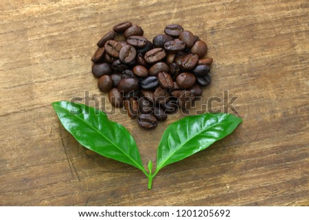 heart shaped roasted coffee beans and leaves, fair trade concept image isolated on wooden background