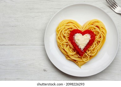 Heart shaped spaghetti with tomato sauce and parmesan cheeses on white plate with white wood background.Romantic vegetarian art food idea for Valentine's dinner.Top view.Copy space

