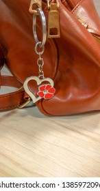 A heart shaped steel key chain with a red flower on it, hanging down on a brown colour ladies bag. 