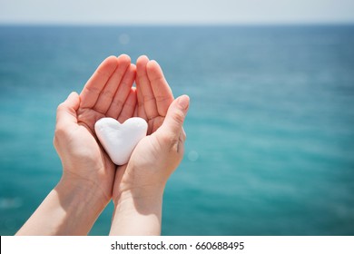 Heart shaped stone held in hands, sea in background - Powered by Shutterstock