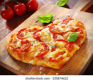 Heart Shaped Vegetarian Pizza Topped With Cheese And Tomato On An Old Wooden Board Signifying Love Of Pizza, Or Romantic Love For Valentines Day Or An Anniversary