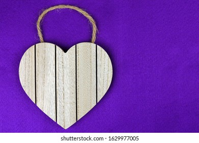 Heart Shaped Wooden Plaque Attached With Hessian String On A Purple Fabric Background.