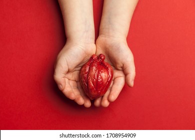 Heart Surgery Concept, Kid Hands Holds Organ On Red Background. Life Saving And Transplantation.