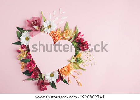 Heart surrounded with fresh colorful flowers on pastel pink background. Creative love layout with copy space. Valentines day, wedding or romantic visual trend. Spring bloom. Flat lay.