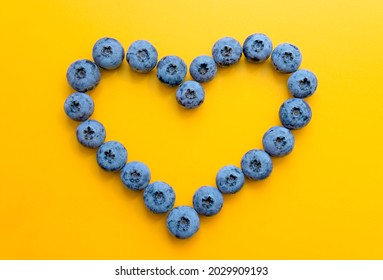 Heart symbol made from blueberries on a yellow background. Heart health concept.