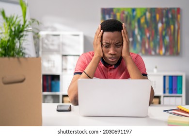 Heartbroken, Sad Boy Sits At Company Desk In Front Of Laptop, Looks Up In Despair, Grabs Head, No Money, Poor Paycheck, Financial Problems, Company Expenses, Horror, Headache, Stress