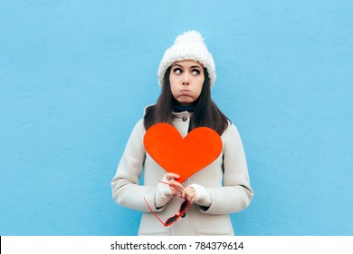 Heartbroken Sad Upset Girl Holding a Heart on Blue Background. Girl feeling blue sad after breakup in time for Valentine’s Day 
