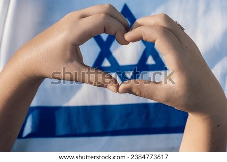 Heartfelt Gesture. Child Forms a Heart with Hands, Framing Magen David On Israeli Flag - Love Israel, Unity, Jewish Identity, Patriotism Symbol.