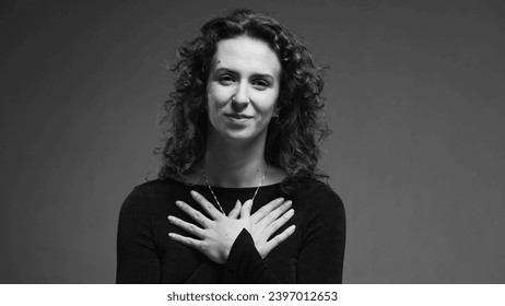 Heartfelt moment of woman putting hands on chest feeling thankful and sincere gratitude in black and white, monochrome