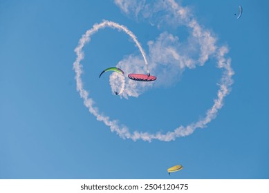 Heartfelt Paragliding Stunt. a paragliding acrobatics performance. Three paragliders are performing daring maneuvers against a backdrop of a clear blue sky. 