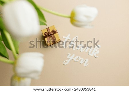 Heartfelt thank you message in cursive script, accompanied by small gift box and soft white tulips on beige background.