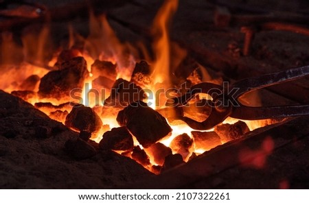 hearth in the forge. a metal tool holds a red-hot piece of iron on fire. before  start forging