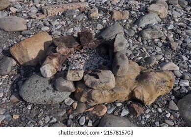 The hearth for the homeless is built of stones on the pebbly bank of the river. Burnt rocks all around. Extinct coals and ashes in the hearth.
