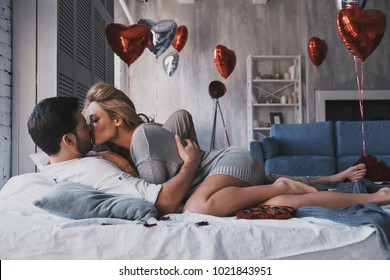 Hearts filled with love.  Beautiful young couple embracing and kissing while lying on the bed at home