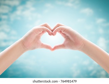 Heart-shape Hand Gesture Of Kid's Body Language For Children's Love, Peace, Kindness, Csr Charity Donation, And World Humanitarian Aid Concept. Hand Isolated On Blur Blue Sky With Cloud