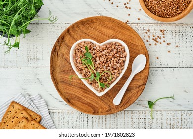 Heart-shaped bowl of boiled buckwheat porridge on old white wooden background. Gluten free ancient grain for healthy diet. Top view. Copy space.