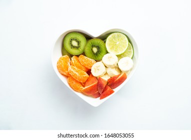 Heart-shaped bowl with fruit isolated on white background. The concept of healthy eating, eating fruit. Bowl with apple, mandarin banana. A bowl filled with fruit. Fruit and vitamins for the heart.