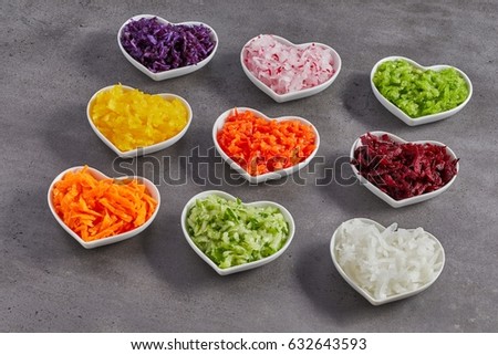 Heart-shaped bowls with grated vegetables as a healthy organic food concept - studio shot from the side over grey background