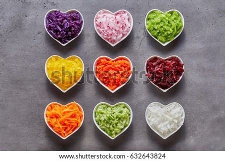 Heart-shaped bowls with healthy grated vegetable ingredients of different colors shot from above on grey background