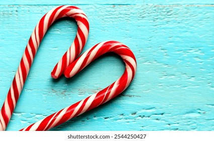 Heart-shaped candy canes on a turquoise wooden background. Two red and white candy canes are arranged to form a heart shape against a textured turquoise wooden surface - Powered by Shutterstock