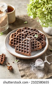 Heart-shaped chocolate waffles as Valentine's Day breakfast, sprinkled with powdered sugar. Vertical orientation