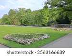 A heart-shaped flowerbed blooming with colorful flowers in a peaceful park, surrounded by lush greenery and vibrant trees on a sunny spring day. Shibden Park, Halifax, West Yorkshire, England, UK.