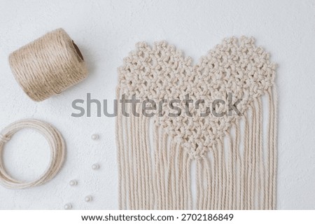 Heart-shaped macrame in progress with tools and jute on white surface