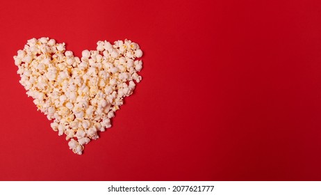 Heart-shaped popcorn on a red background with space for text. Top view. Valentine's Day, cinema time concept. Minimal style.