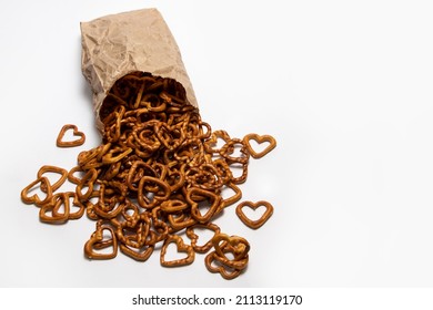 Heart-shaped salty pretzel snacks spilled from the paper bag on white