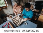 A heartwarming moment of a grandmother teaching her grandson to bake pastries in a cozy kitchen setting. They are preparing dough on a baking tray, fostering family bonding and culinary skills.