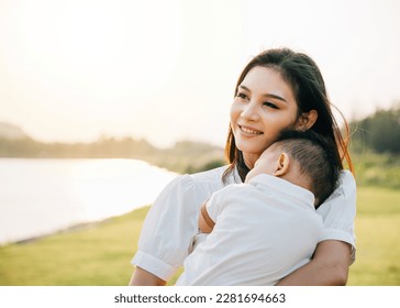 A heartwarming Mother's Day moment captured in the park at sunset. Beautiful mother cradles her sleeping baby, basking in peaceful nature and lovingly smiling at her newborn. Family care at its finest - Shutterstock ID 2281694663