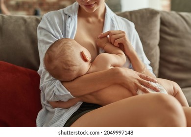 Heartwarming Portrait Of Young Mother Nursing Her Sweet Baby Holding Its Hand. Mom Feeding Naked Child To Provide Skin Contact. Intimate Process In Comfort Of Home.