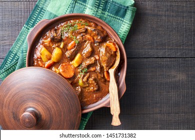 Hearty beer and lamb stew, with potato, carrot, stewed in a dark beer, with thyme stems, served in a clay pot with irish soda bread on a wooden background, top view, copy space - Shutterstock ID 1451731382