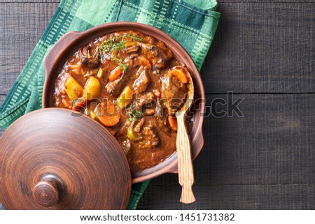 Hearty beer and lamb stew, with potato, carrot, stewed in a dark beer, with thyme stems, served in a clay pot with irish soda bread on a wooden background, top view, copy space