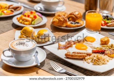 Hearty breakfast spread featuring eggs, bacon, sausage, hash browns, coffee, fresh fruit, croissants, juice on wooden table, perfect for brunch or relaxation concept.