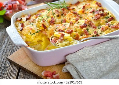 Hearty potato gratin with parmesan cheese, cream and delicious cured bacon from South Tyrol freshly served from the oven on a wooden table