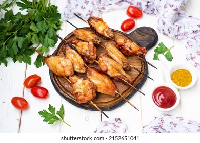 A Hearty Snack For The Whole Family: Delicious Grilled Chicken Wings With Spices On Skewers On A White Background. Close-up