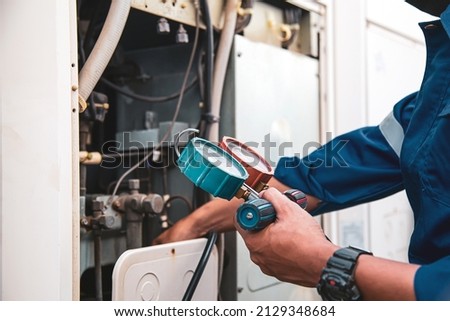 Heat and Air Conditioning, HVAC system service technician using measuring manifold gauge checking refrigerant and filling industrial air conditioner after duct cleaning maintenance outdoor compressor.