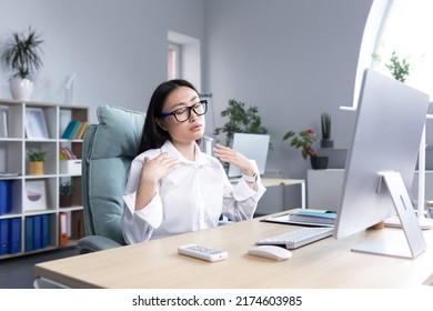 Heat In The Office, Asian Woman Trying To Freshen Up, Business Woman Working At The Computer, Waving Her Hands To Cool Down.