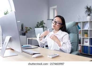 Heat In The Office, Asian Woman Trying To Freshen Up, Business Woman Working At The Computer, Waving Her Hands To Cool Down.